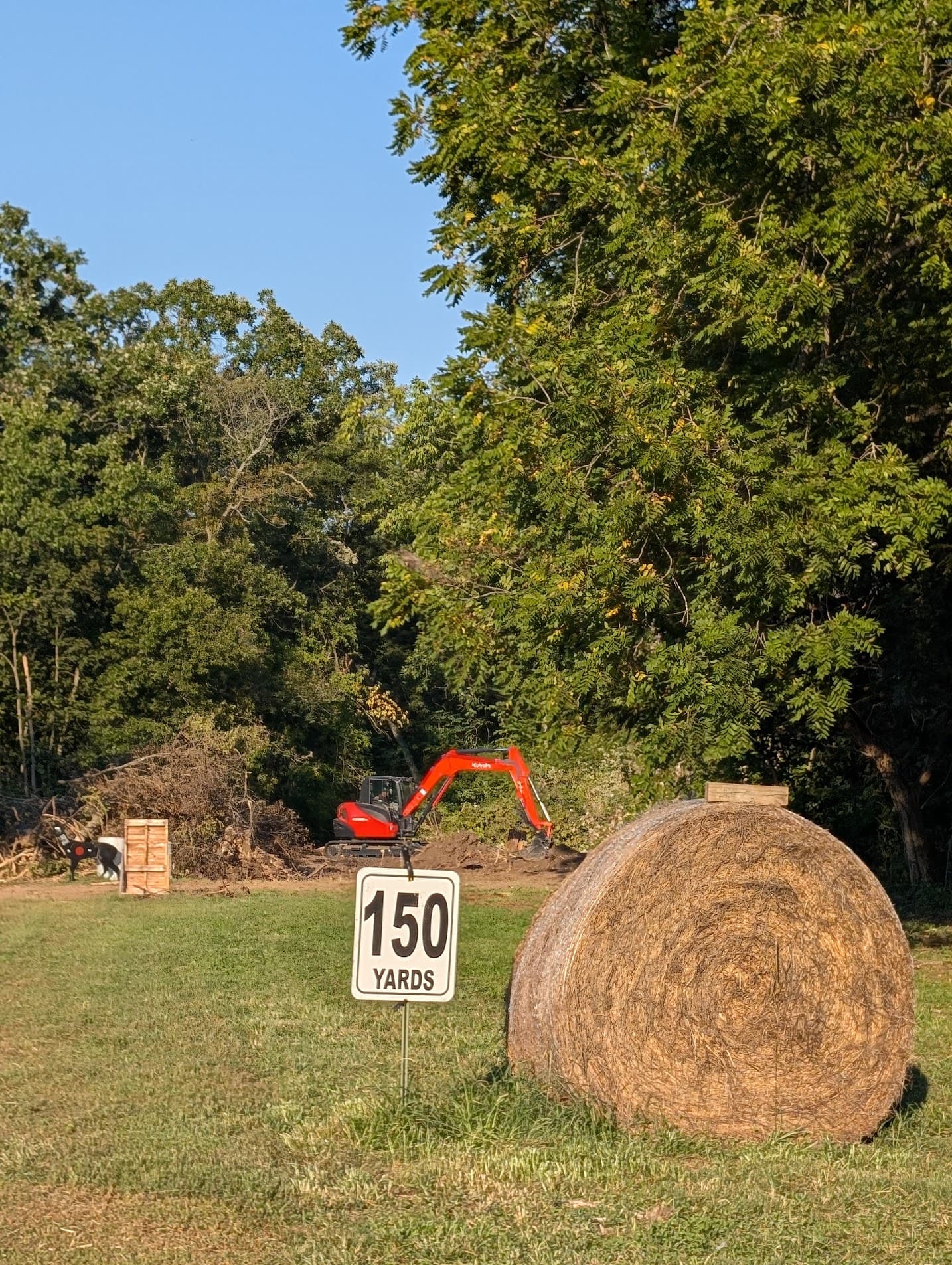 The 150-yard marker on the rifle line beside a round hay bale, with an excavator working downrange to extend the line